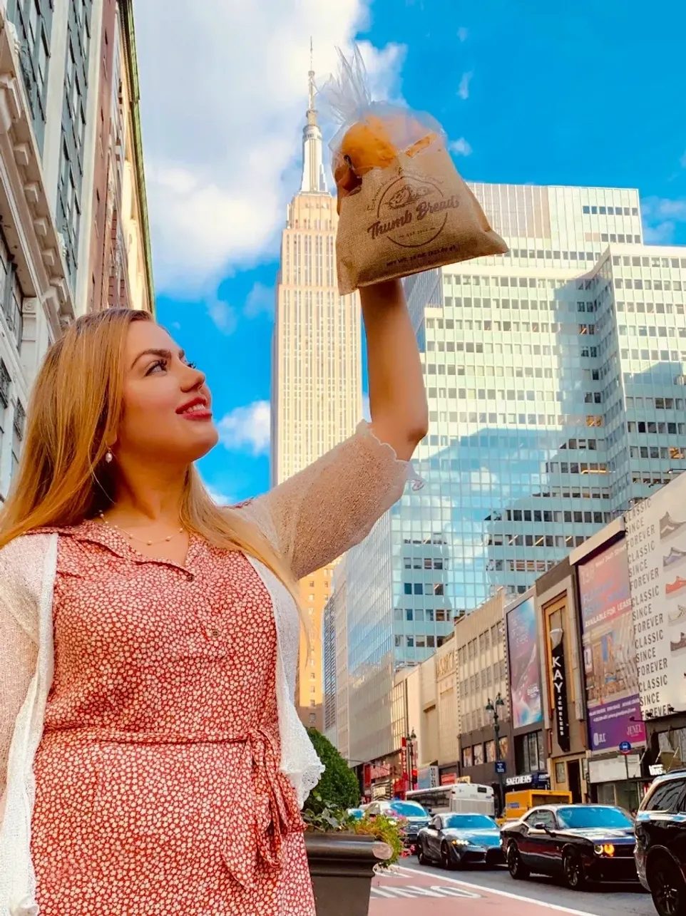 Arzu Esendemir holding up Thumb Bread® in its burlap bag in front of the Empire State Building