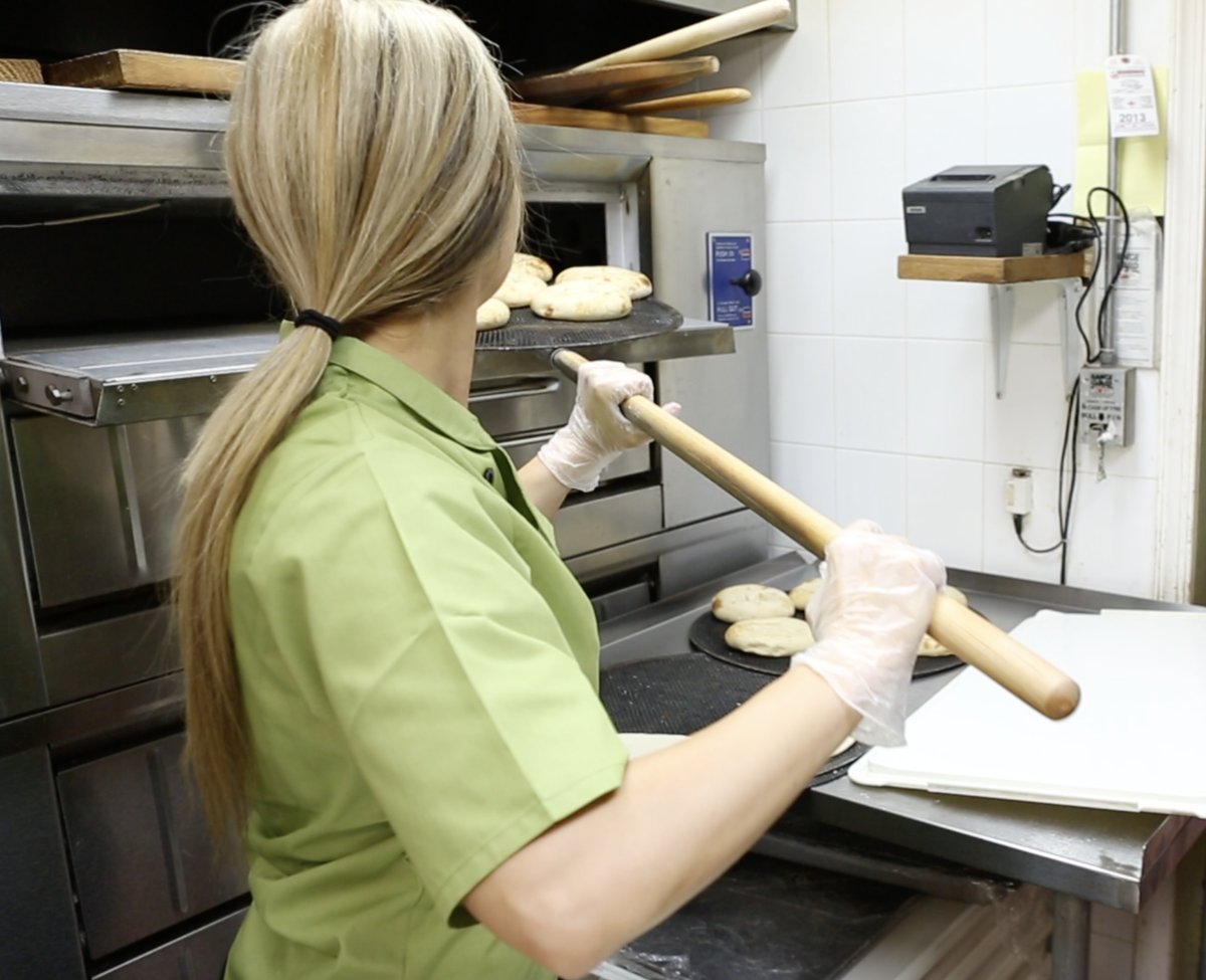 One of the Esendemir sisters loading flatbreads into the oven with a peel